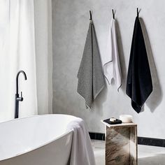 a white bath tub sitting next to two black towels hanging on the side of it