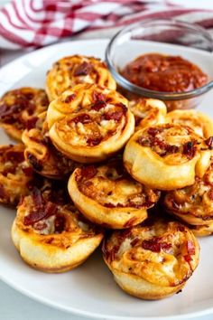 some small pizzas on a white plate next to a bowl of ketchup