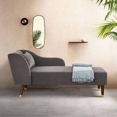 a gray couch sitting in front of a mirror on a wall next to a potted plant