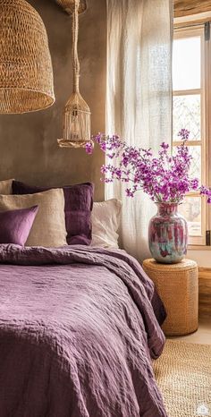 a bed with purple linens and pillows in a bedroom next to a large window