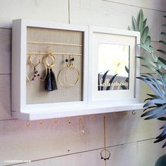 a white shelf with two framed pictures and earrings hanging from it's sides next to a potted plant