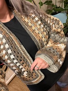 a woman wearing a crocheted jacket sitting on a couch with her hand in her pocket