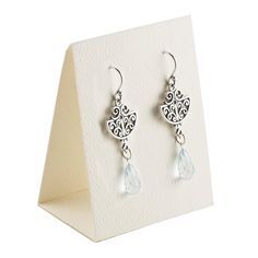 a pair of earrings sitting on top of a white display stand next to a card