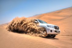 a white car driving through the desert with sand blowing around it's front wheels