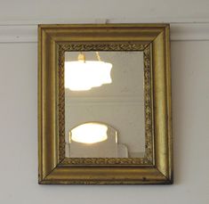 a gold framed mirror hanging on the side of a wall next to a light fixture