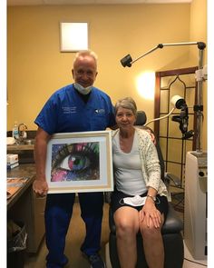 a man and woman pose for a photo in front of an eyeball framed photograph