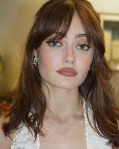 a close up of a woman with long hair wearing earrings and a white top, looking at the camera