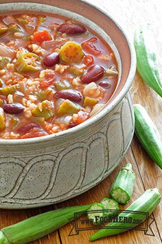 a bowl filled with beans and vegetables on top of a wooden table next to green peppers