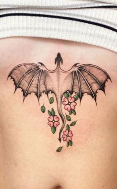 a woman's stomach with flowers and a bat tattoo on her side ribcage