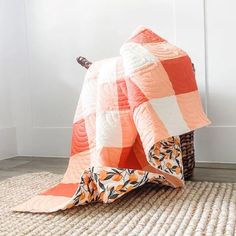 an orange and white quilt sitting on top of a rug next to a basket filled with flowers