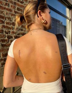 a woman with tattoos on her back standing in front of a brick wall and looking out the window