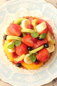 a white plate topped with fruit salad on top of a blue and white doily