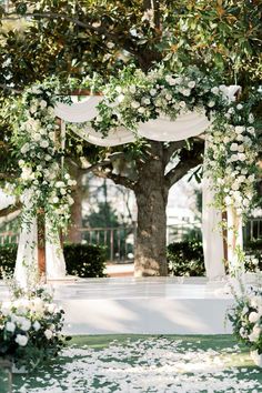 an outdoor wedding ceremony with white flowers and greenery on the ground under a tree