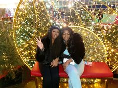 two women are sitting on a bench in front of a christmas tree with lights behind them