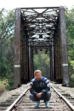 a man kneeling down on train tracks in front of an old metal bridge over water