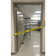 an empty hallway with yellow caution tape on the floor and shelves in the back ground