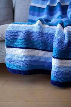 a blue and white crocheted blanket sitting on top of a wooden floor next to a couch