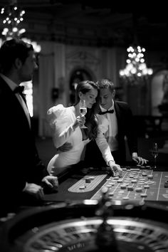 a man and woman at a casino roule with drinks in their hands, while the man is holding a glass of wine