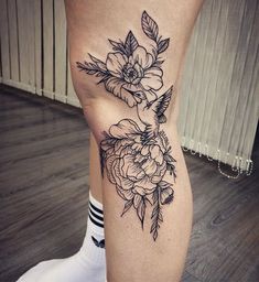 a woman's leg with flowers on it and a black outline tattoo in the middle