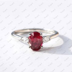 a ring with a red stone and two white diamonds on the side, sitting on a table