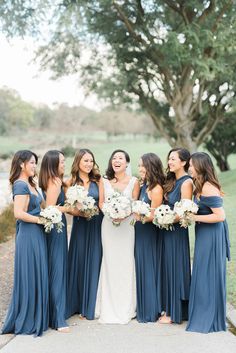 a bride and her bridesmaids laughing together in front of a tree at their wedding