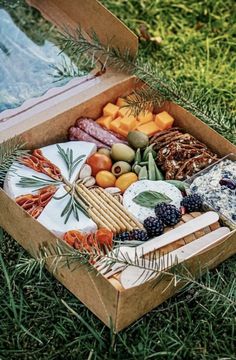 a wooden box filled with assorted cheeses and meats on top of grass