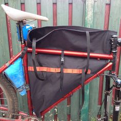 a bicycle with a bag attached to the front and back seat, parked next to a fence