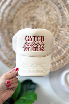 a woman holding up a white trucker hat with the words catch negatives not feelings