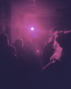 a group of people standing in a dark room with red light coming from the ceiling