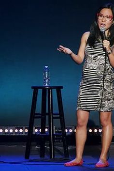 a woman standing in front of a microphone with her hand out to the side while wearing red shoes