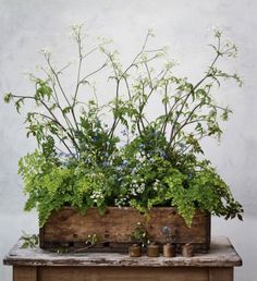 an arrangement of flowers and greenery in a wooden box on top of a table