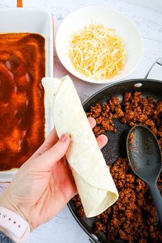 a person holding a tortilla in their hand next to some chili and cheese