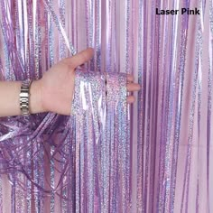 a hand is holding onto some purple tinsel fringes that are hanging from the ceiling