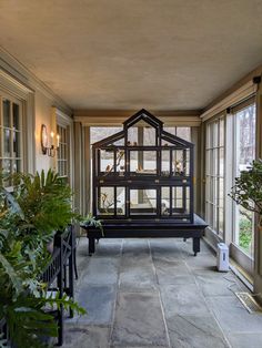 a house model sitting on top of a bench in a room filled with potted plants