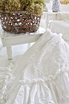 a white bed sitting next to a basket with flowers in it on top of a table