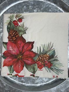 a christmas napkin with pine cones and poinsettis on it sitting on a silver plate