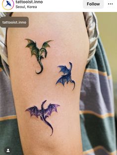 two dragon tattoos on the left arm and one is purple with green wings, while the other