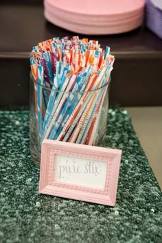 there are many different colored straws in a glass cup with a sign next to it