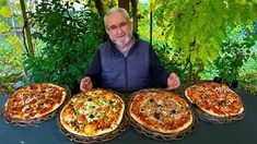 a man sitting at a table with four different pizzas on baskets in front of him