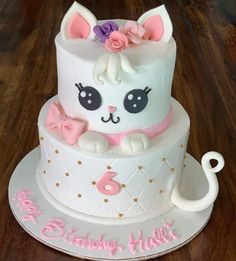 a birthday cake with a cat on top and pink bow around the edges, sitting on a wooden table