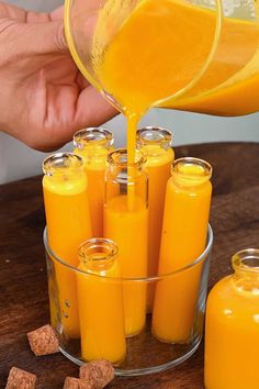 a person pouring orange juice into small glass containers on a wooden table next to some brown sugar cubes