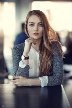 a woman sitting at a table with her hand on her chin and looking off to the side