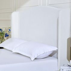 a white bed with two pillows on top of it next to a book shelf and flowers