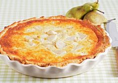 a pie sitting on top of a table next to a knife and some pears