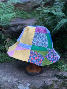 a colorful hat sitting on top of a wooden stand in front of some trees and bushes