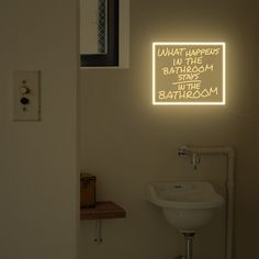 a bathroom with a sink, mirror and neon sign above it that says what happens in the bathroom stays to the bathroom