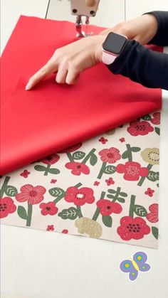 someone is using a sewing machine to sew on a red piece of paper with flowers