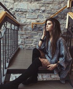 a woman is sitting on the stairs talking on her cell phone and looking off into the distance