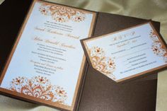 an open brown and white wedding card on top of a black folder with gold trim