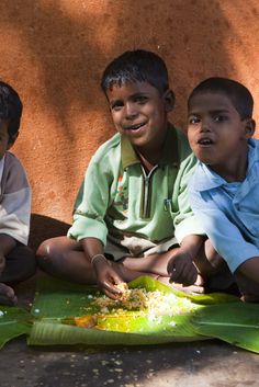 three young boys sitting on the ground next to each other and making something with food